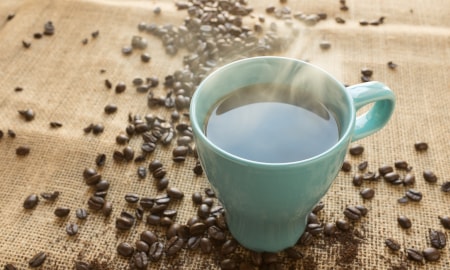 Mug of steaming hot coffee surrounded by coffee beans